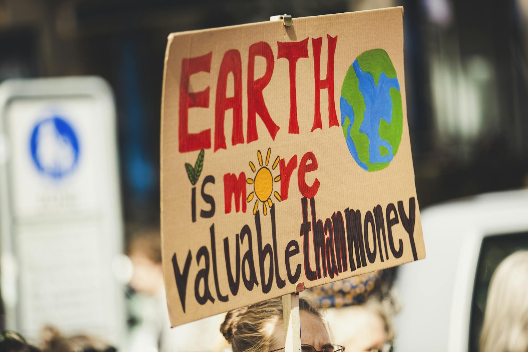 Sign reading 'Earth is more valuable than money' at a climate protest outdoors.